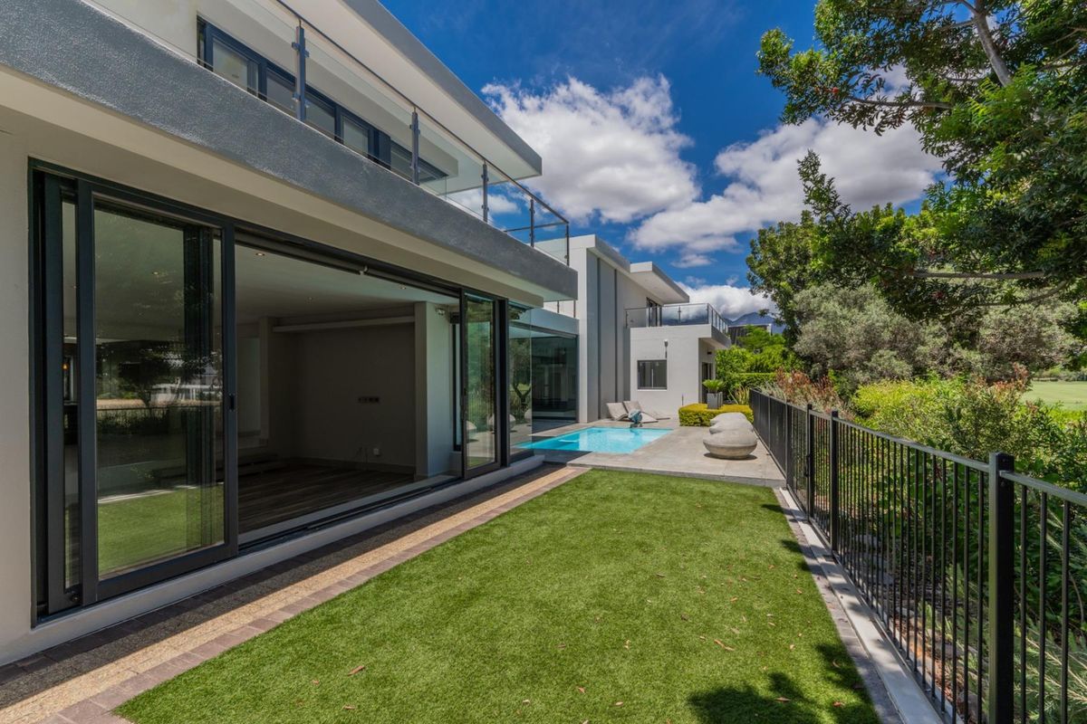 Modern rear exterior featuring a swimming pool, paved patio area, artificial lawn, and large sliding glass doors opening into the home.