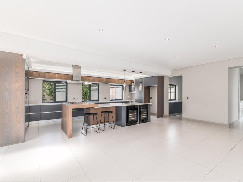 Modern open-plan kitchen featuring a large island with stone countertops, integrated wine coolers, gas hob, and sleek wood-toned cabinetry with recessed lighting.