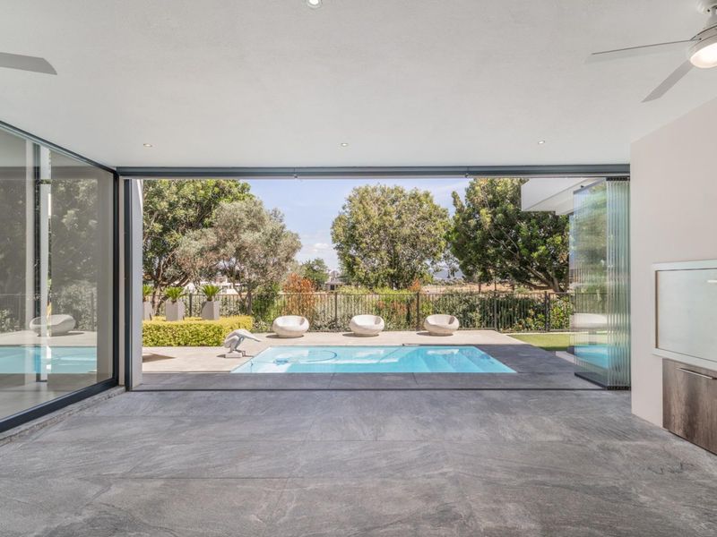 Spacious covered patio featuring large sliding glass doors, tiled flooring, and recessed lighting, seamlessly connecting to an outdoor swimming pool and garden area.