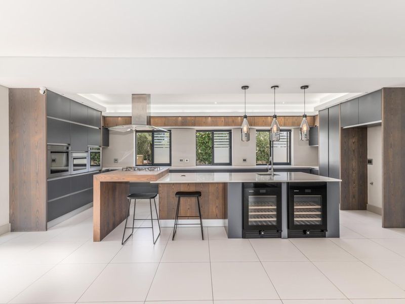 Modern, high-end kitchen featuring a large island, integrated appliances, wine coolers, and premium wood and matte cabinetry with sleek tiled flooring.