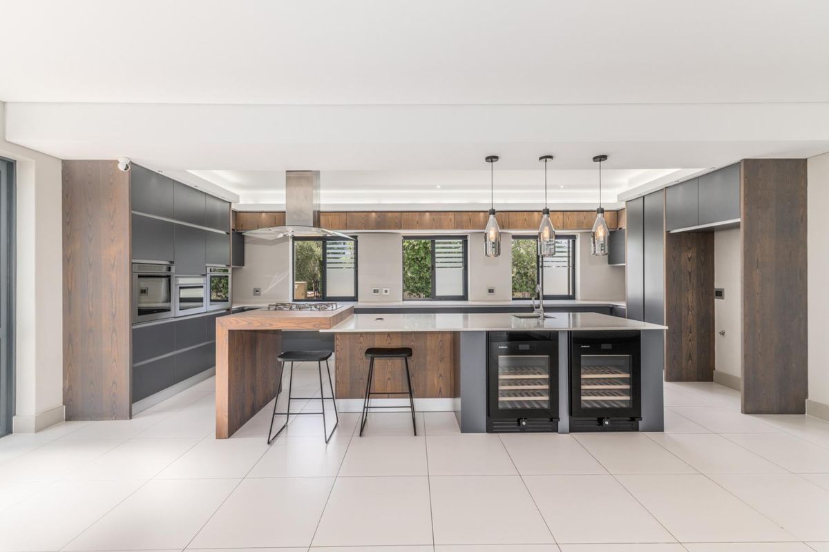 Modern, high-end kitchen featuring a large island, integrated appliances, wine coolers, and premium wood and matte cabinetry with sleek tiled flooring.