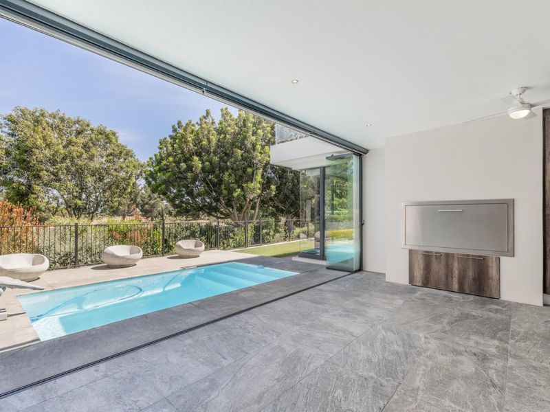 Modern covered patio featuring large format floor tiles, a built-in braai, and seamless sliding doors opening directly onto a private swimming pool area.