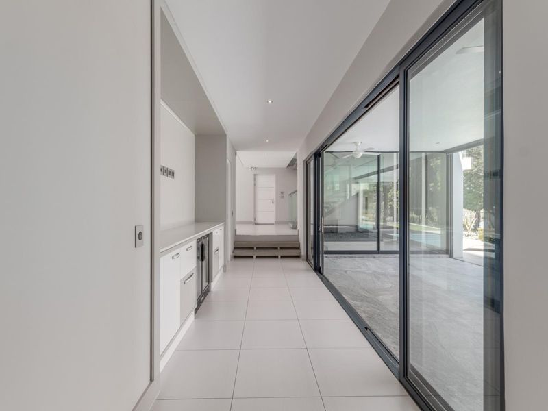A bright, modern hallway featuring sleek built-in cabinetry, large-format floor tiles, and expansive sliding glass doors that provide seamless access to the outdoor area.