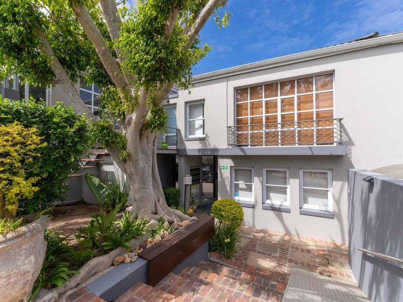 A well-maintained exterior courtyard area featuring brick paving, mature trees, and a balcony with decorative metal railing.