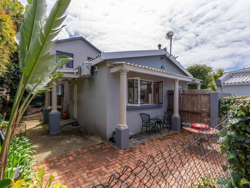 Rear exterior view of the house featuring a covered patio area with classic columns, brick paving, and an integrated air conditioning unit.
