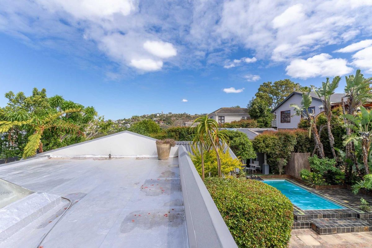 Elevated view overlooking a private garden with a swimming pool and lush landscaping, captured from a flat roof section.