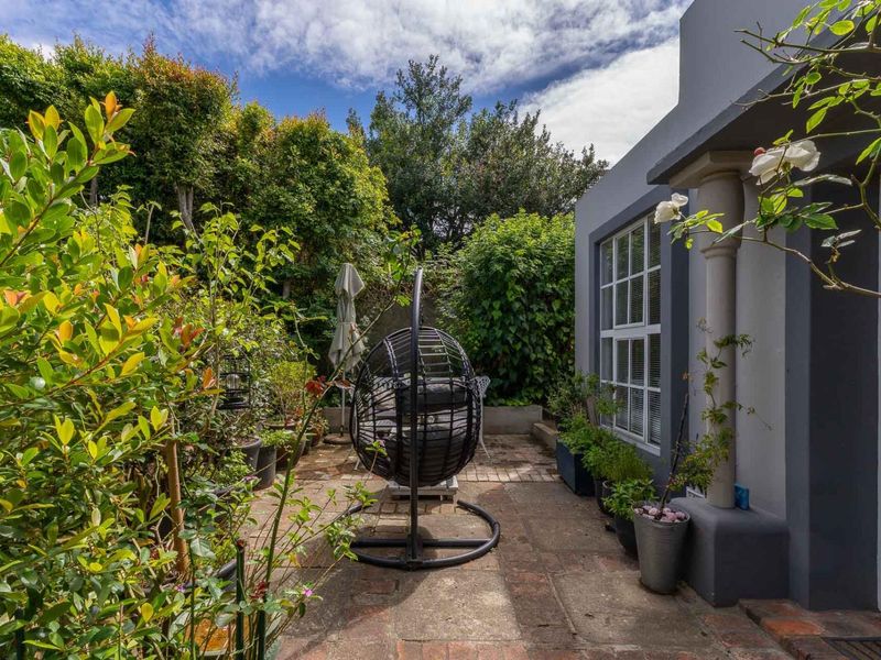 A private rear courtyard featuring brick paving, established garden greenery, and direct access to the home through glass-paned doors.