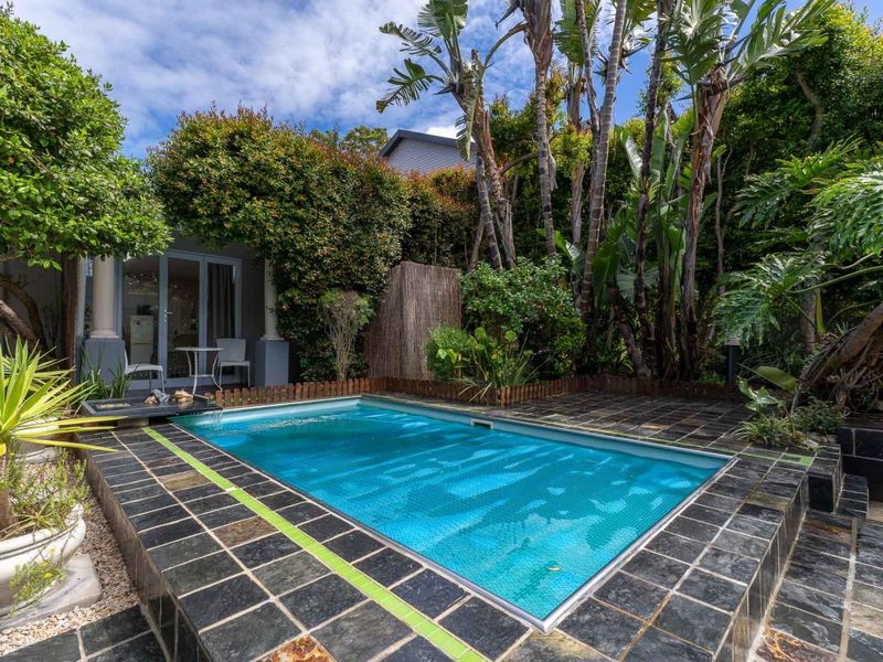 A private outdoor pool area featuring dark stone tiling, lush established garden landscaping, and direct access to the home via glass sliding doors.