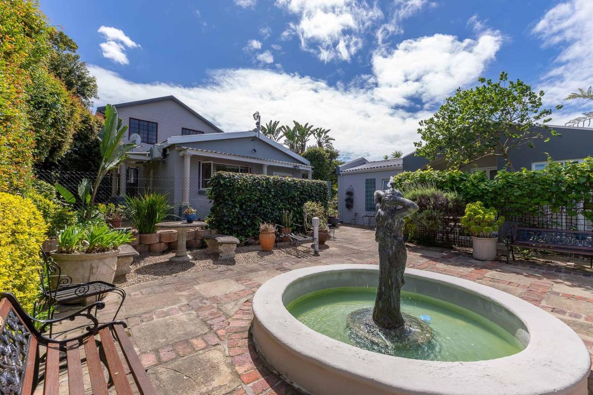 A landscaped rear garden featuring a central stone fountain, paved patio area, and established greenery surrounding the main dwelling.