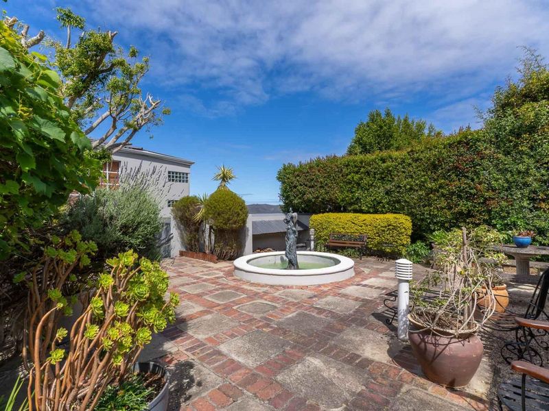 A private rear garden featuring a central stone fountain, brick-paved patio area, and established perimeter hedging.