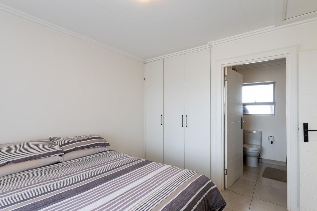 A bright bedroom featuring built-in cupboards and an en-suite bathroom with a toilet and window.