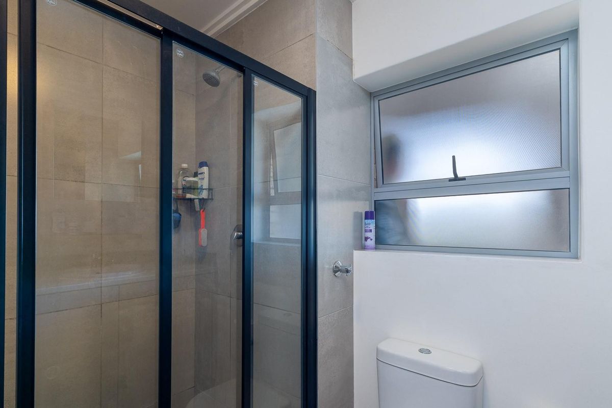 Modern bathroom featuring a glass-enclosed shower with black framing, tiled walls, and a white toilet under a frosted window.