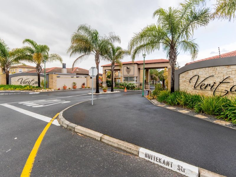 The entrance to Veritas estate featuring a secure gatehouse, stone-clad signage walls, and well-maintained paved access roads.