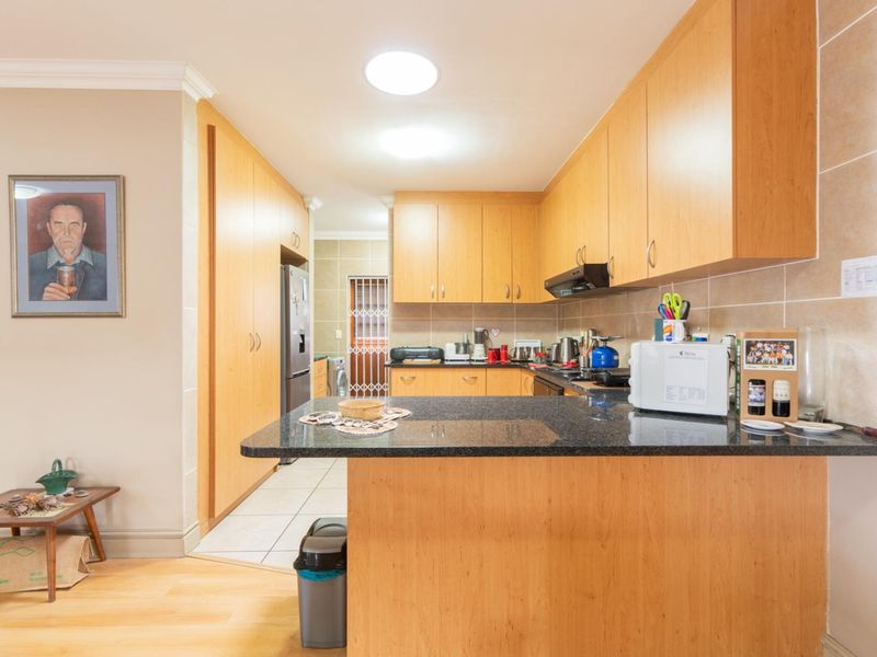 A functional kitchen featuring light wood cabinetry, granite countertops, and a tiled backsplash, with an open-plan layout connecting to the adjacent living area.