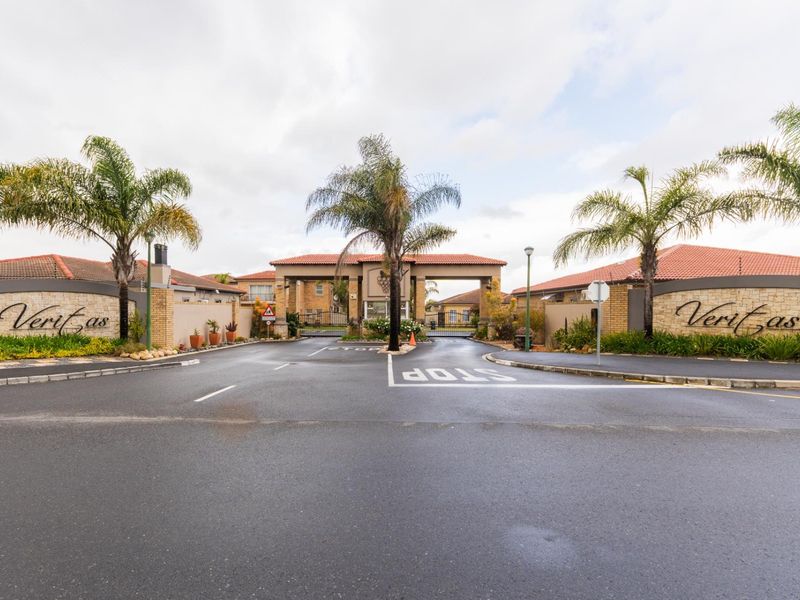 The entrance to Veritas estate featuring a secure gated access point, paved driveway, and landscaped brick boundary walls.