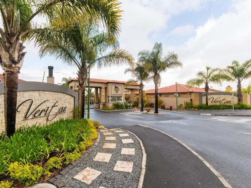 The entrance to Veritas estate featuring a secure gatehouse, stone-clad signage, paved driveway, and well-maintained landscaped gardens.