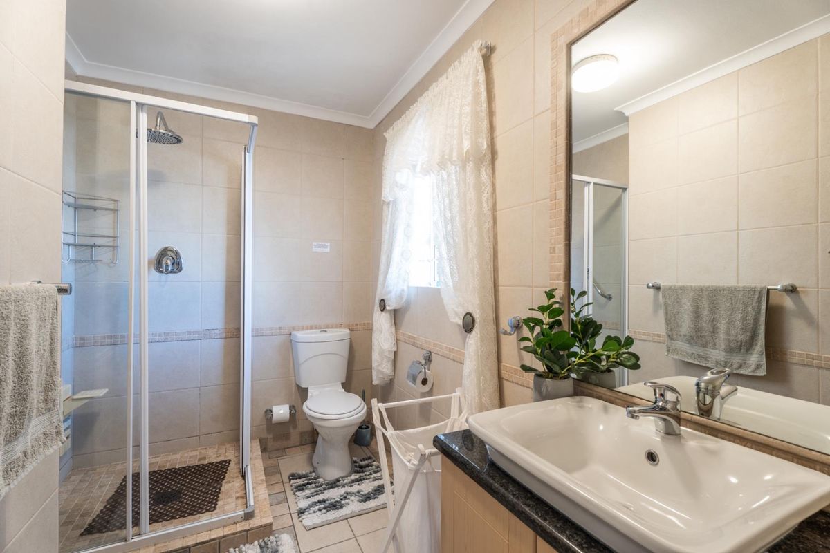 A functional bathroom featuring a glass-enclosed shower, a vanity with a stone countertop, a toilet, and neutral wall tiling.