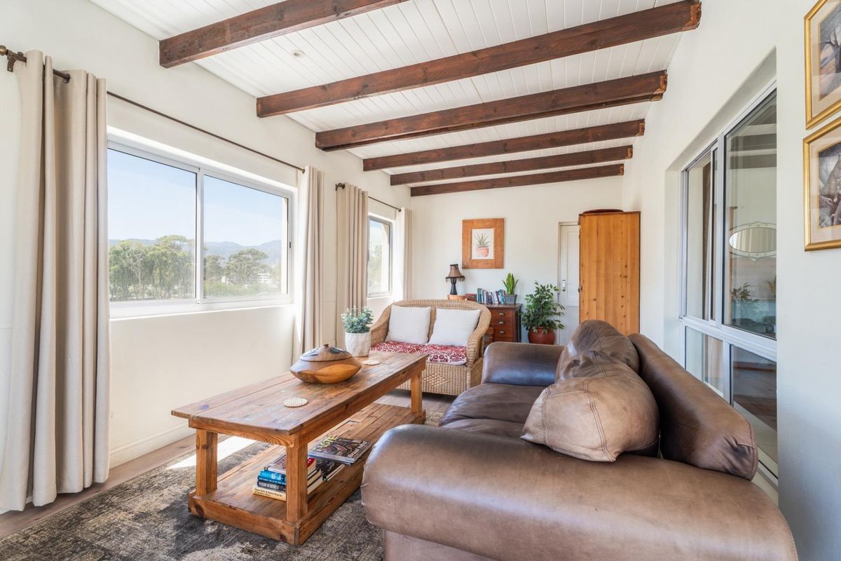 A bright living room featuring exposed timber ceiling beams, large windows with natural light, and neutral wall finishes.