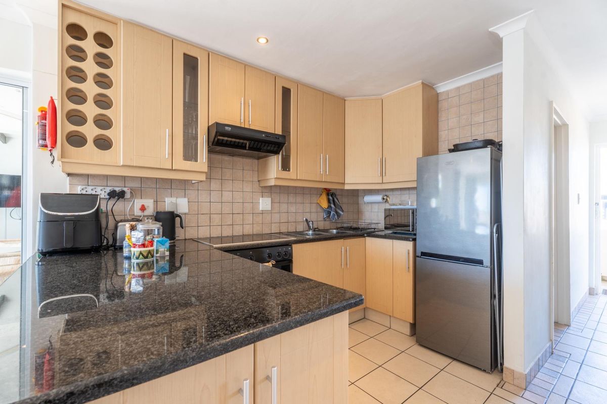 Functional kitchen featuring light wood cabinetry, dark granite countertops, tiled backsplash, and integrated extractor fan, offering a practical layout for daily cooking.