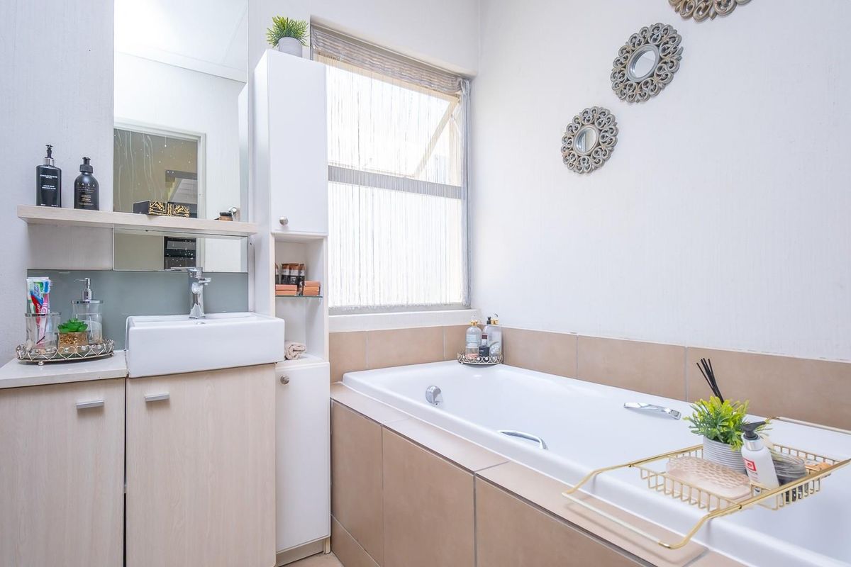 A well-maintained bathroom featuring a built-in bathtub with tiled surround, a modern vanity with integrated basin, and a tall storage cabinet.