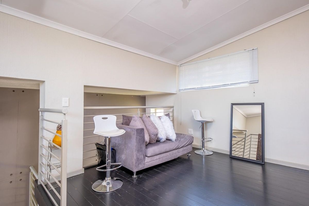 A loft-style living area featuring dark timber flooring, a metal balustrade, and a horizontal window with fitted blinds.
