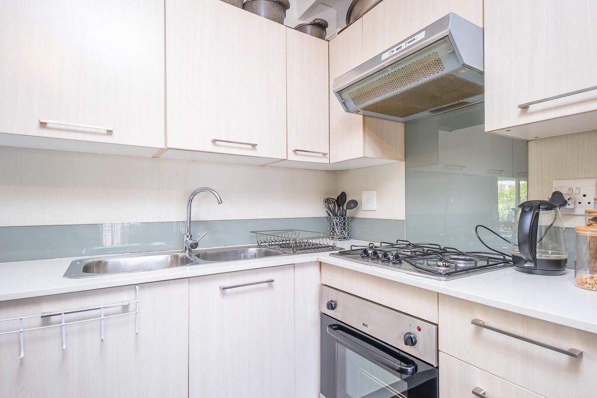Compact kitchen featuring light wood-grain cabinetry, a stainless steel sink, built-in gas hob, oven, and a glass splashback.