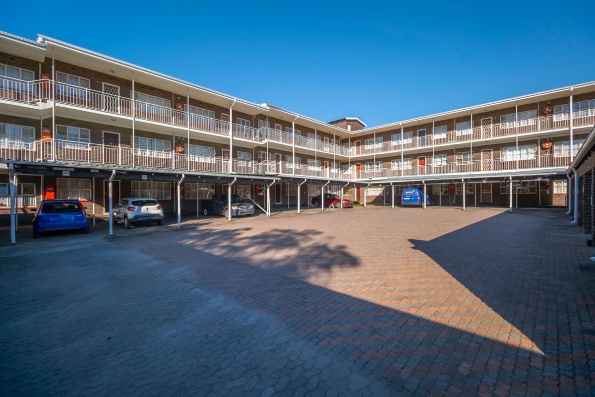 Exterior view of a multi-story apartment complex featuring covered parking bays and open-air walkways on each level.