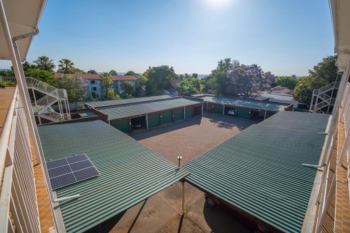 Elevated view of the apartment complex parking area, featuring multiple garage units, covered parking bays, and solar panels on the roof.