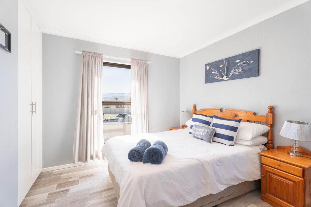 A bright and well-maintained bedroom featuring light-toned laminate flooring, a built-in wardrobe, and neutral wall finishes.