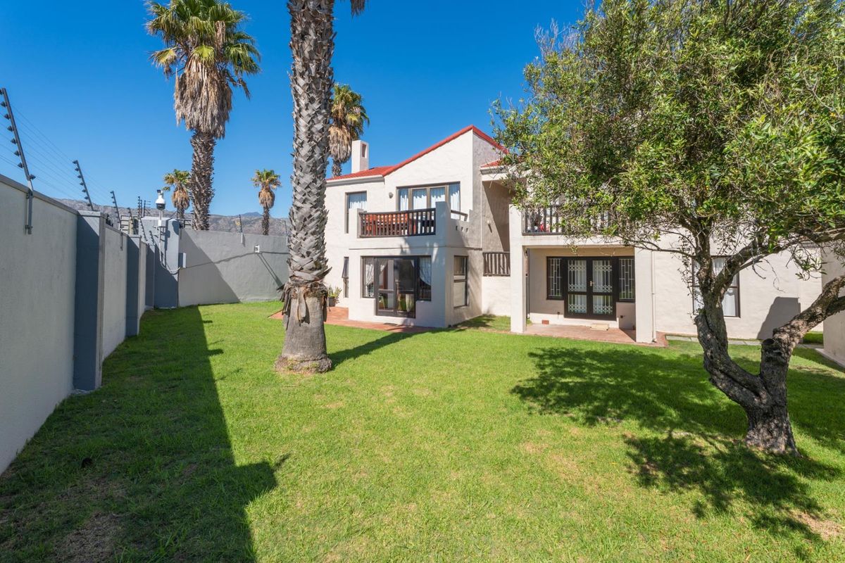 Rear view of the apartment building featuring a private garden, lawn, patio area, and upper-level balconies with secure perimeter fencing.