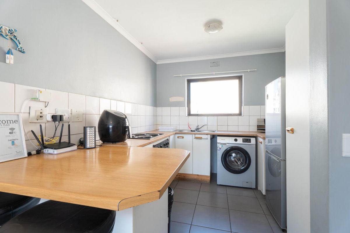 Functional kitchen featuring built-in cabinetry, tiled backsplash, integrated hob and oven, breakfast counter, and tiled flooring with space for laundry appliances.