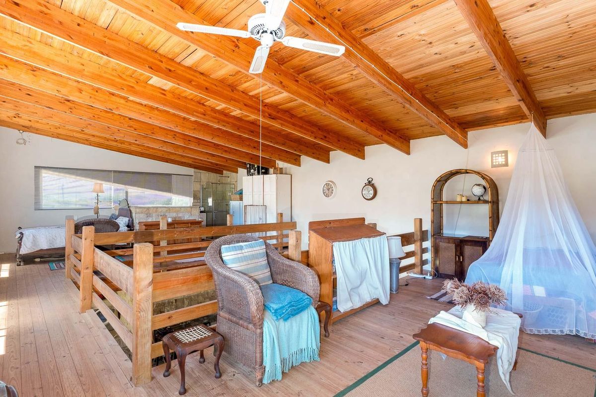 Spacious loft-style bedroom featuring exposed timber beams, vaulted wood ceiling, and a ceiling fan, offering a rustic and open living environment.