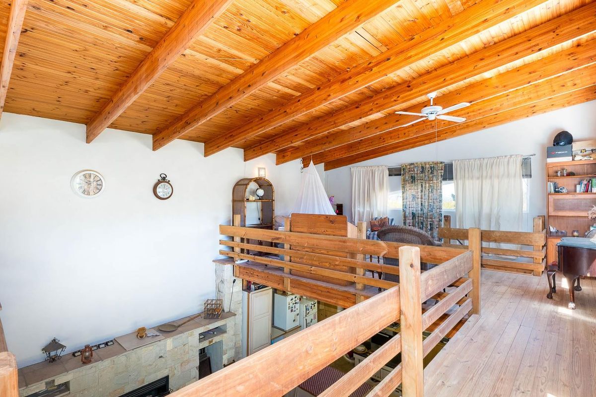 A spacious mezzanine level featuring exposed timber beam ceilings, wooden balustrades, and timber flooring, overlooking the main living area below.
