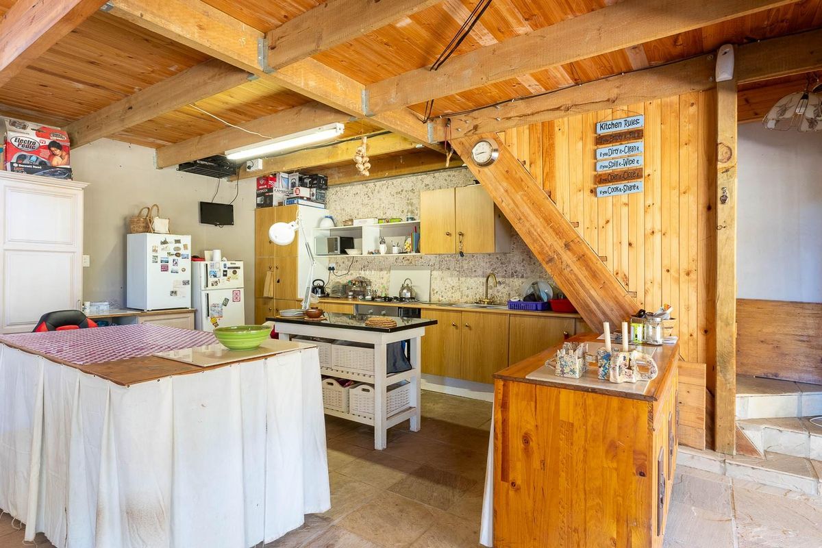 Rustic kitchen featuring exposed timber ceiling beams, wooden wall paneling, stone flooring, and built-in cabinetry with integrated sink and cooktop.