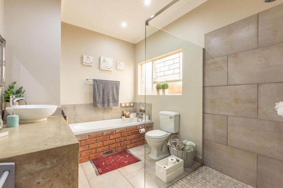 A modern bathroom featuring a brick-clad bathtub, a glass-enclosed walk-in shower with tiled walls, a pedestal basin, and a toilet.