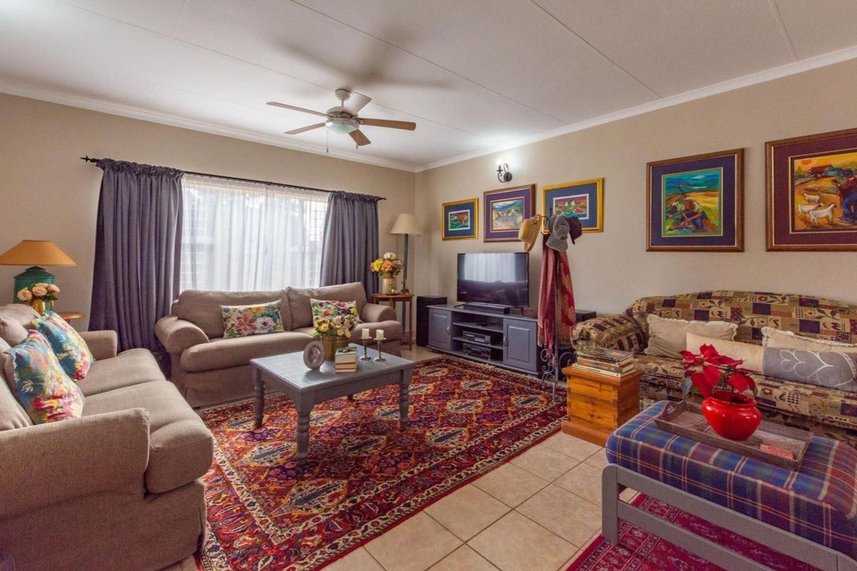 A comfortable living room featuring tiled flooring, a ceiling fan, and large windows with curtains, providing a functional and inviting space.