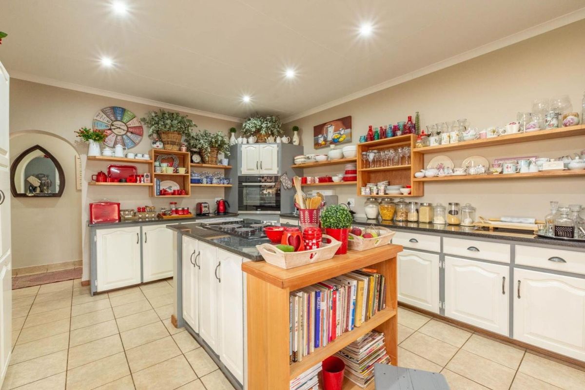 A functional kitchen featuring a central island, built-in oven, gas cooktop, and extensive open shelving for storage, finished with tiled flooring and recessed lighting.