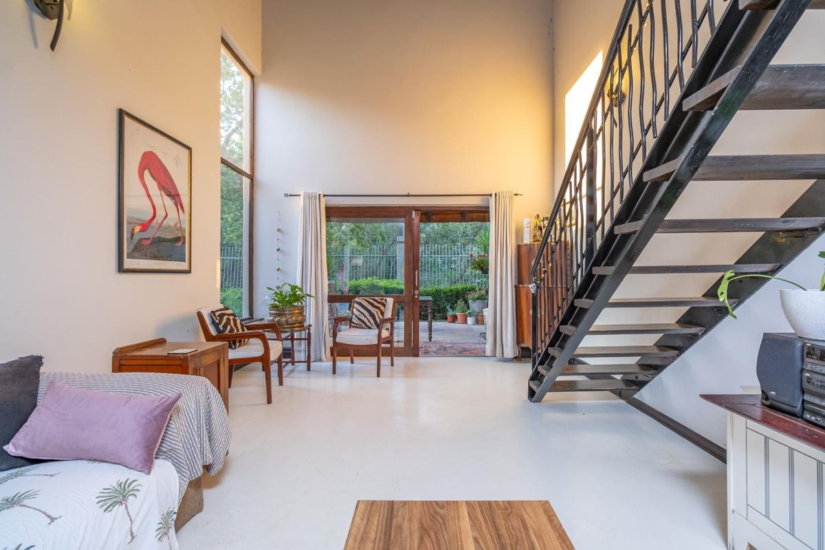 Spacious living area featuring double-volume ceilings, large windows, and a metal staircase leading to the upper level, with direct access to the patio.