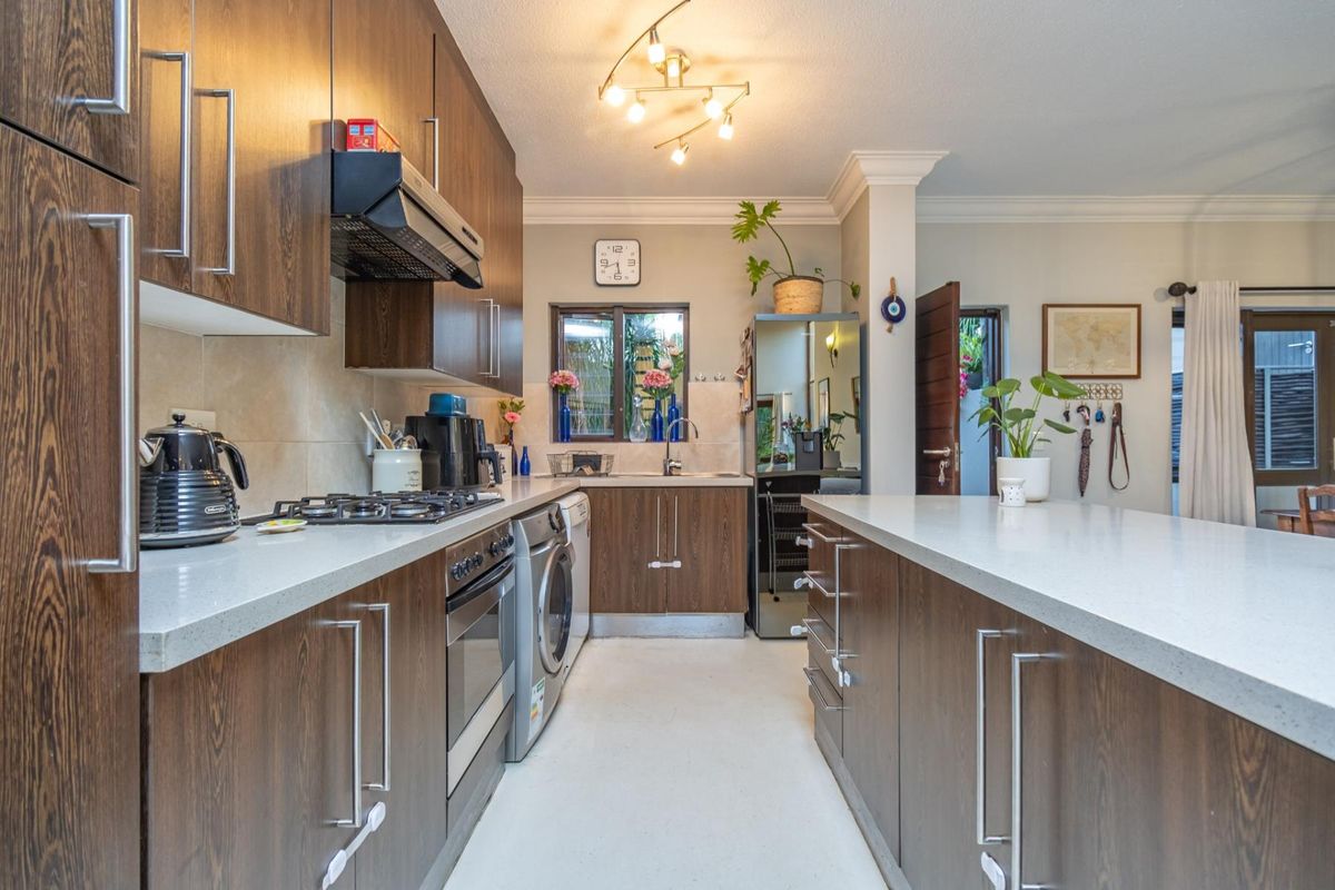 Modern kitchen featuring dark wood cabinetry, stone countertops, a gas hob, built-in oven, and a central island, providing a functional and stylish workspace.