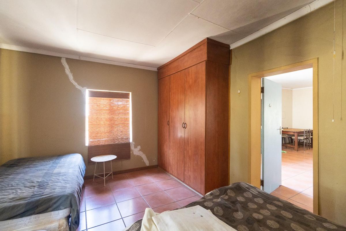 A bedroom featuring built-in wooden cupboards and tiled flooring, currently showing signs of significant wall cracking and plaster damage.