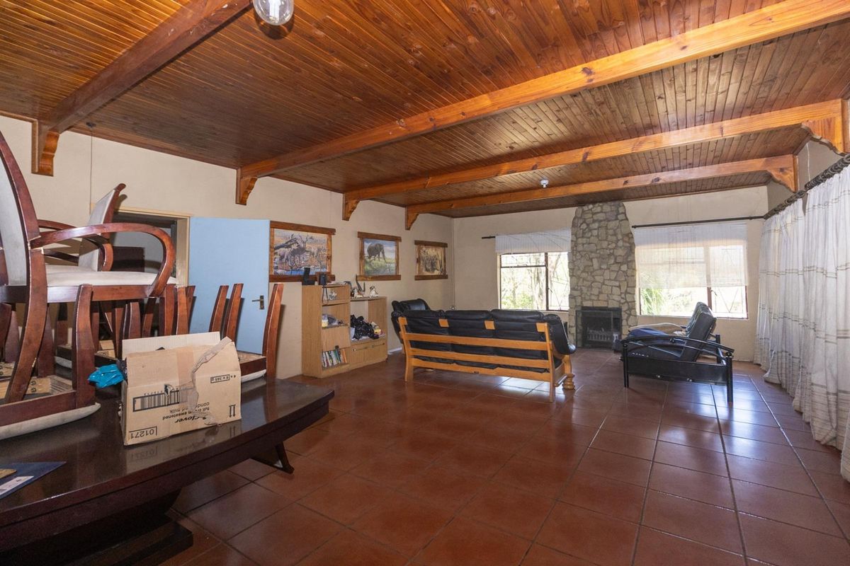 Spacious living room featuring a rustic stone fireplace, exposed timber beam ceiling, and terracotta floor tiles.