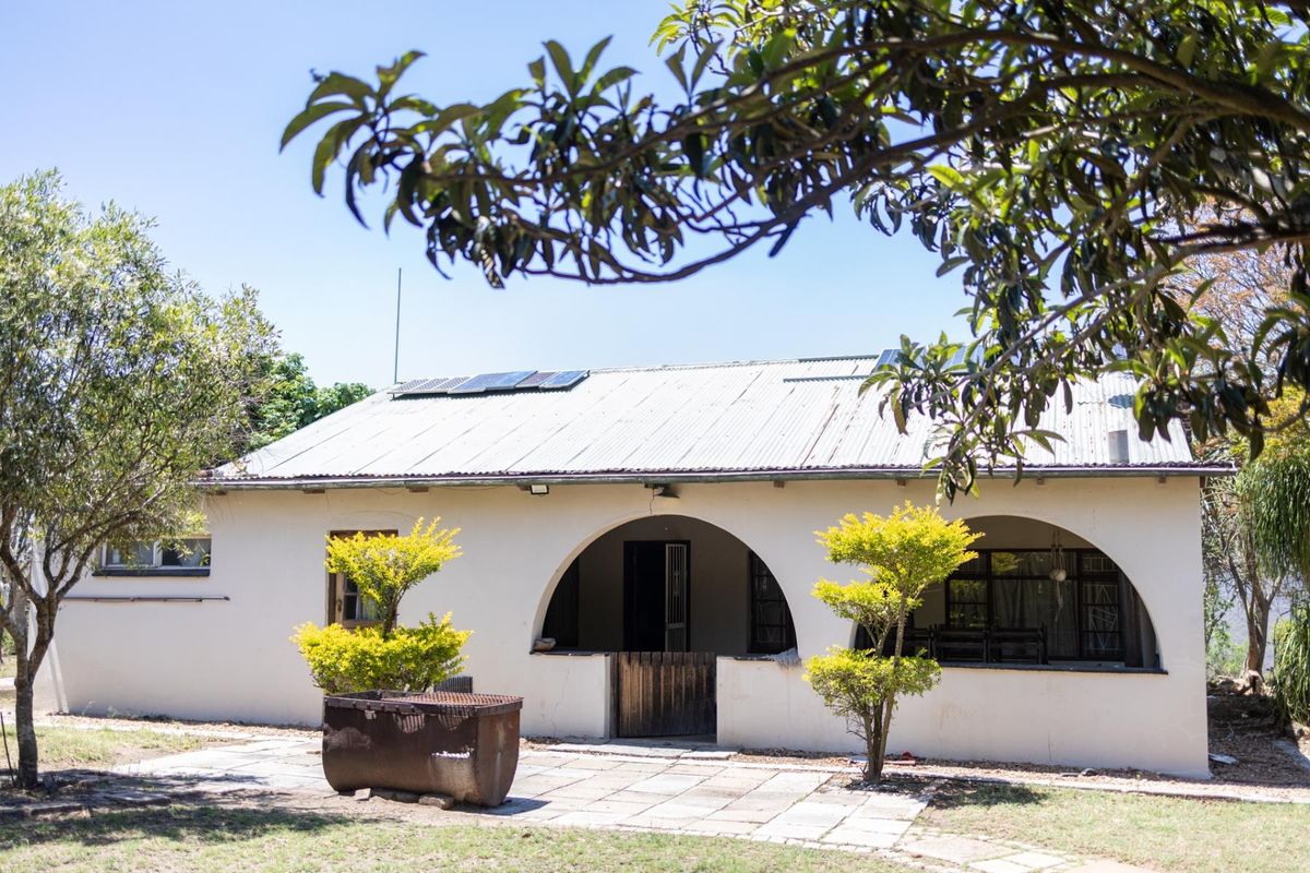 A charming farm-style residence featuring a covered arched patio, corrugated metal roof with solar panels, and a paved outdoor area.