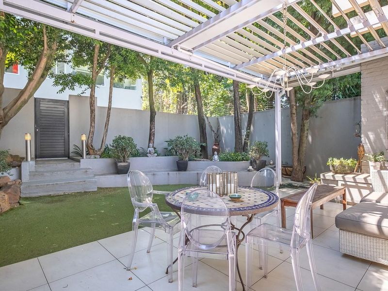 A well-maintained covered patio area featuring tiled flooring, a louvre roof system, and tiered garden landscaping with built-in retaining walls.