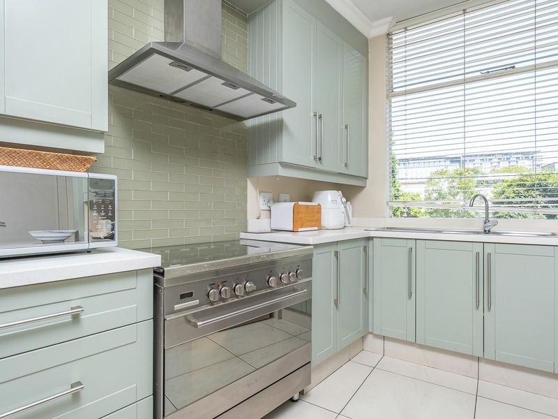 Modern kitchen featuring light green cabinetry, stainless steel appliances, subway tile backsplash, and stone countertops with ample natural light.