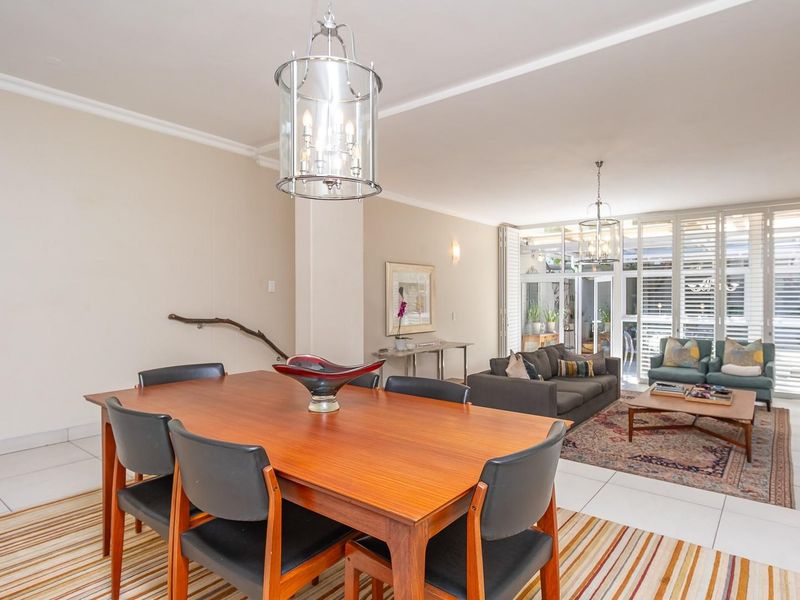 Spacious open-plan living and dining area featuring tiled floors, elegant pendant lighting, and large folding glass doors leading to an outdoor space.