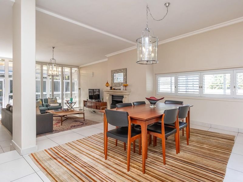 Spacious open-plan living and dining area featuring tiled flooring, a central fireplace, and plantation shutters, creating a bright and well-maintained living space.