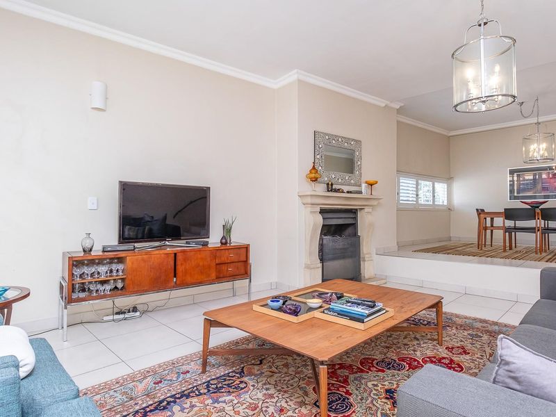 Spacious open-plan living and dining area featuring tiled flooring, a central fireplace, and a raised dining platform with elegant pendant lighting.