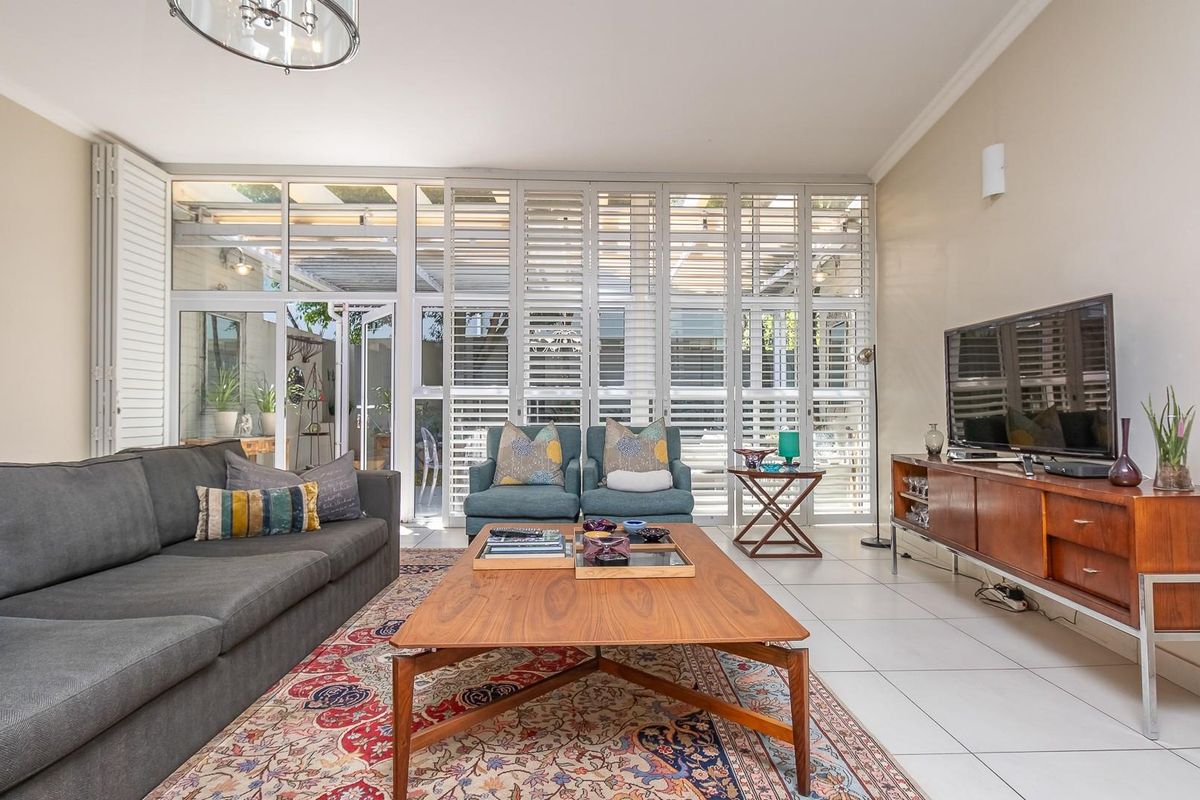 A bright and spacious living room featuring large glass sliding doors with white plantation shutters, leading out to a covered patio area.