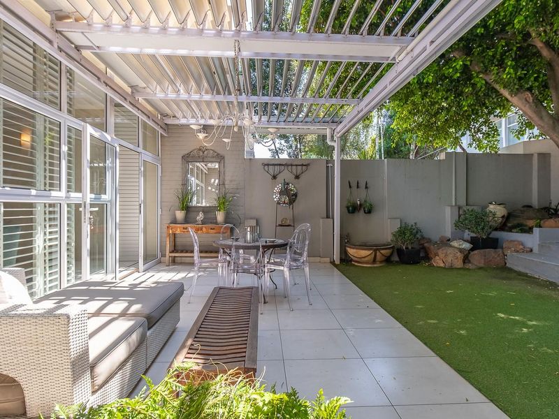 A well-maintained covered patio featuring a retractable louvered roof, tiled flooring, and seamless access to a landscaped garden area with artificial turf.