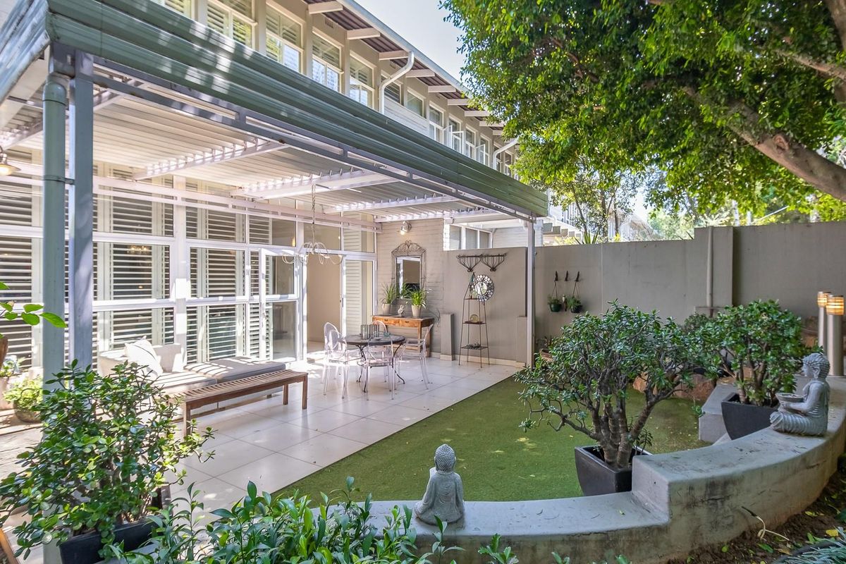 A well-maintained rear patio area featuring tiled flooring, a covered pergola structure, and a landscaped garden with a low concrete retaining wall.